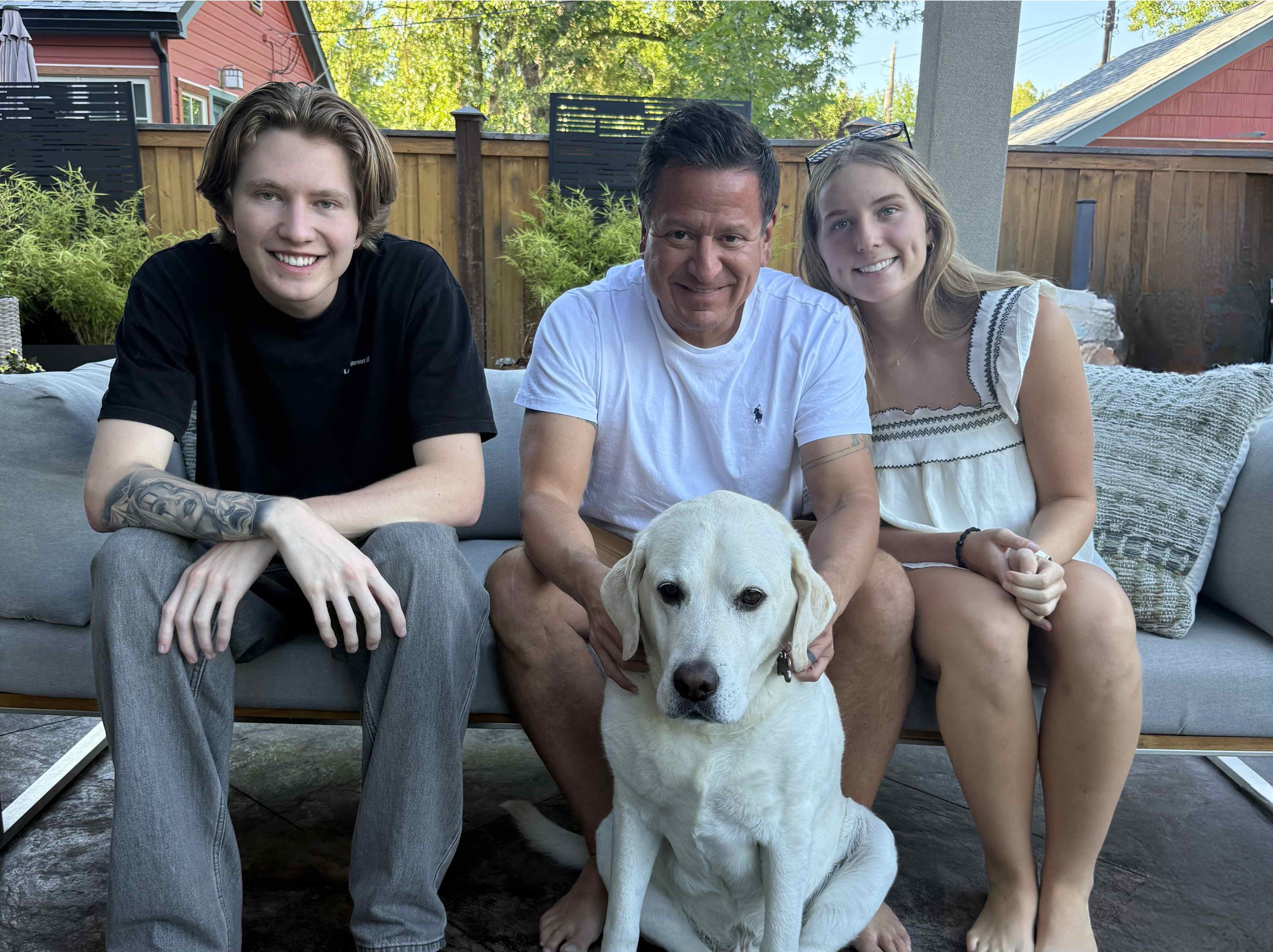 A father with his two grown children and the family dog in a sunlit backyard